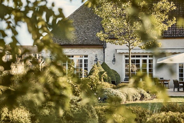 A building with a white facade, large windows, and a tree in the foreground. - COMO Le Montrachet (Puligny-Montrachet)