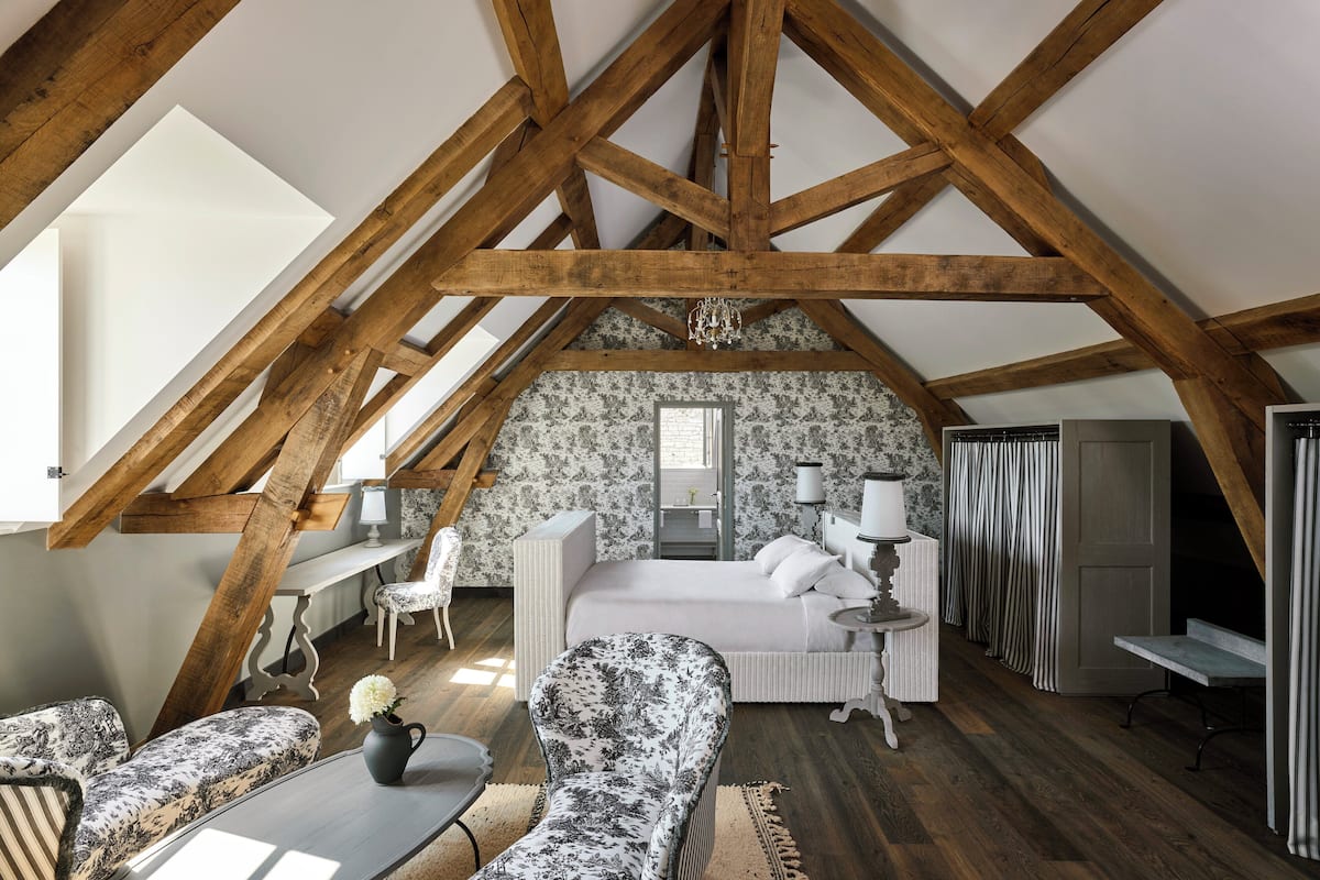 A bedroom with a sloped ceiling, wooden beams, a bed, a desk, and a chair.