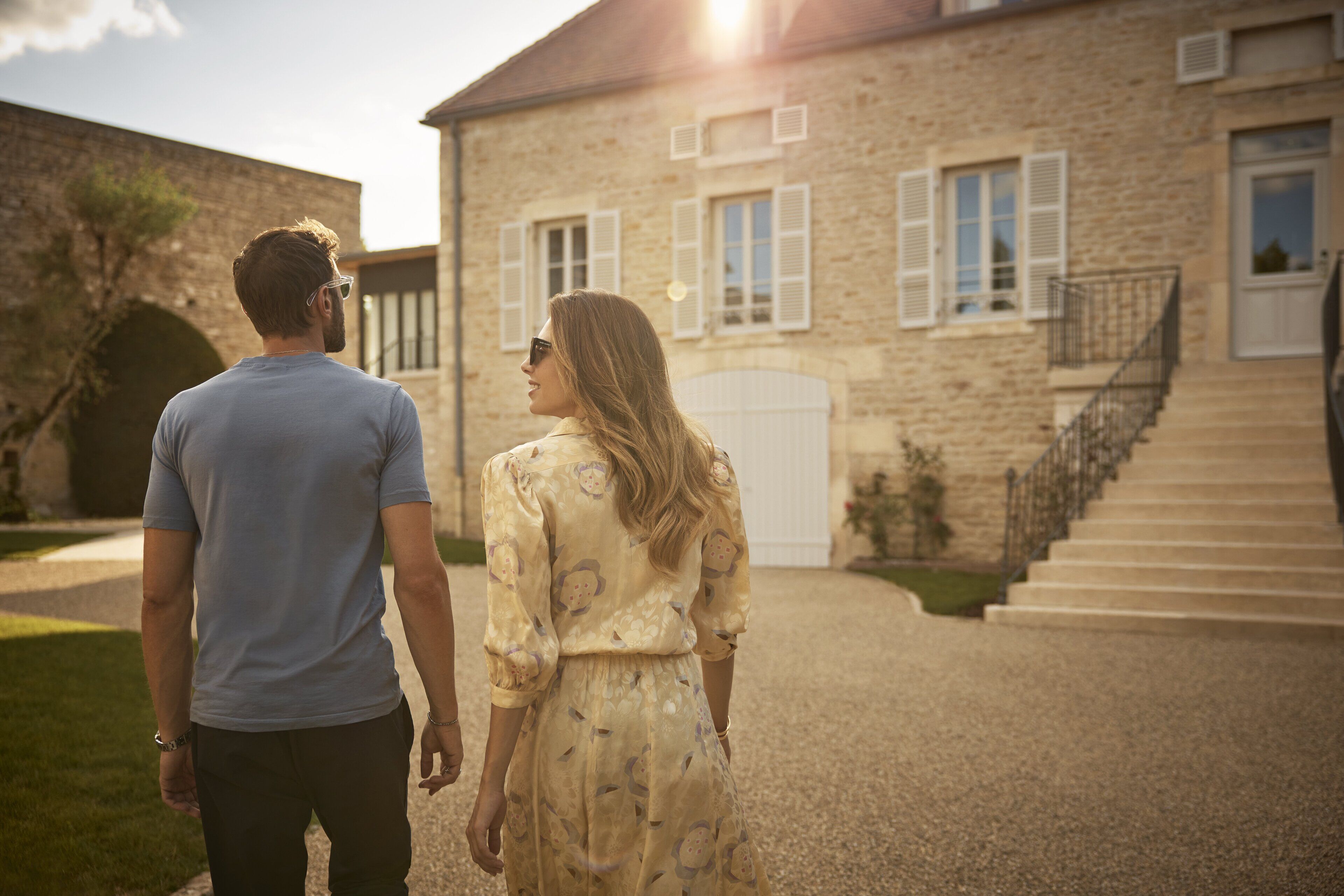 Um casal caminhando em direção a um edifício de pedra com escadas e uma porta branca.