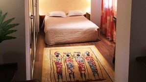 A hotel room with a bed, a nightstand, a wall-mounted picture, and a patterned rug. - HOTEL Les Peyrières (Olemps)