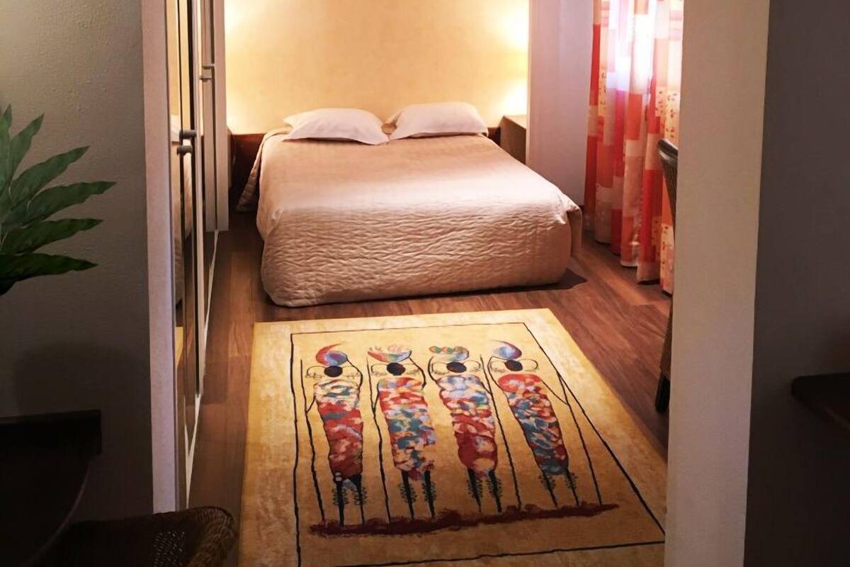 A hotel room with a bed, a nightstand, a wall-mounted picture, and a patterned rug.