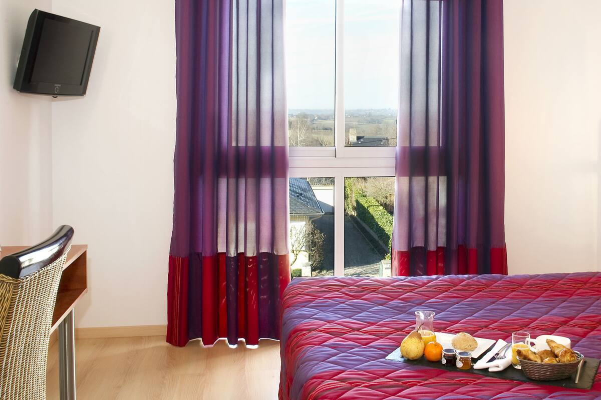 A hotel room with a bed, a desk, a chair, a television, and a window with curtains.