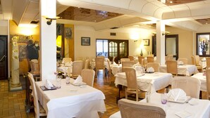 A restaurant with multiple tables and chairs, white tablecloths, and a brick floor. - HOTEL Les Peyrières (Olemps)