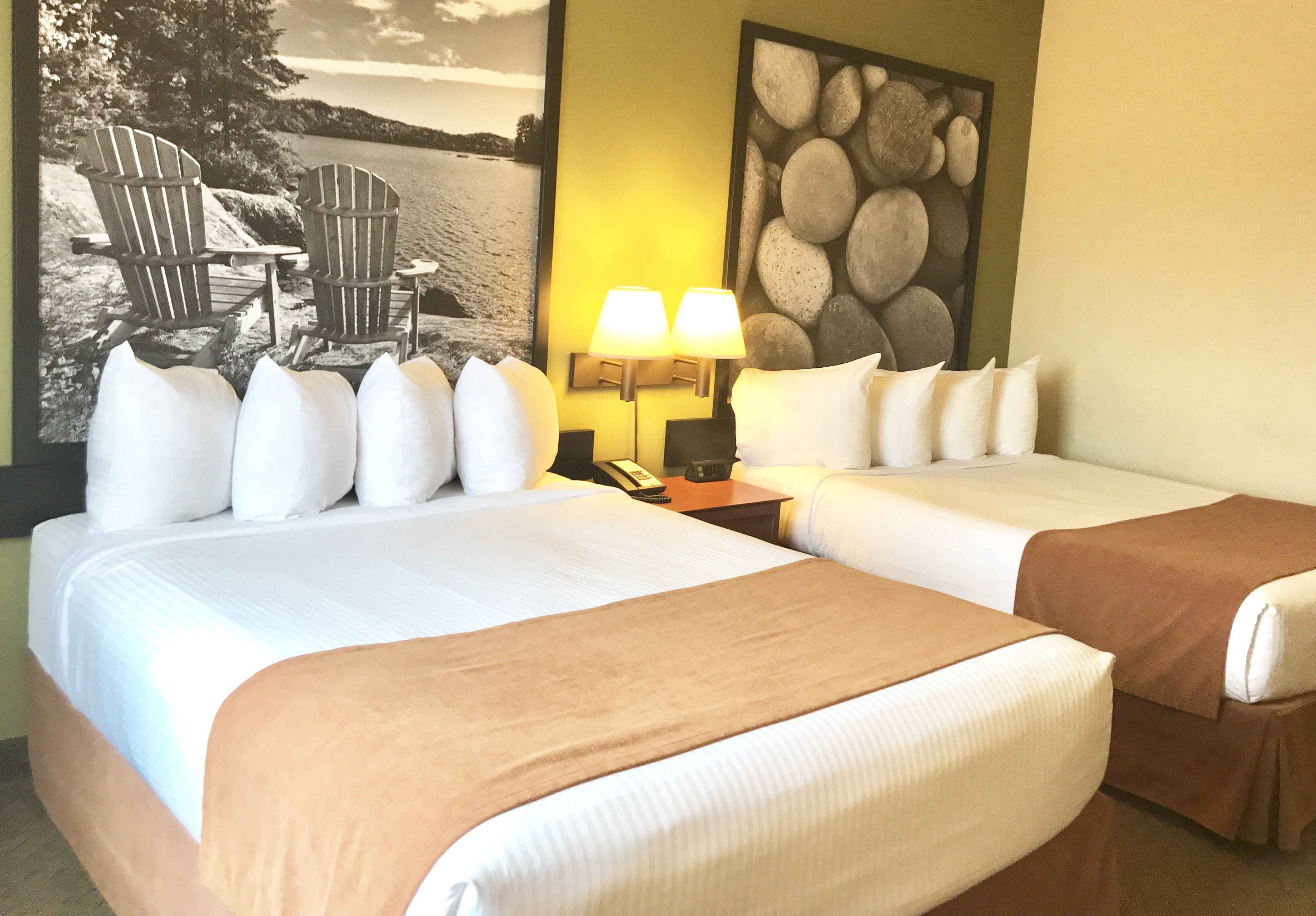 A hotel room with two beds, a painting of a beach scene, a lamp, and a telephone on the nightstand.