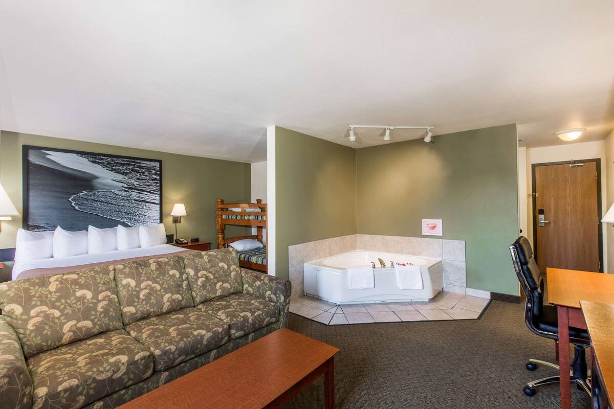 A hotel room with a bed, a sofa, a bathtub, a desk, and a large painting on the wall.