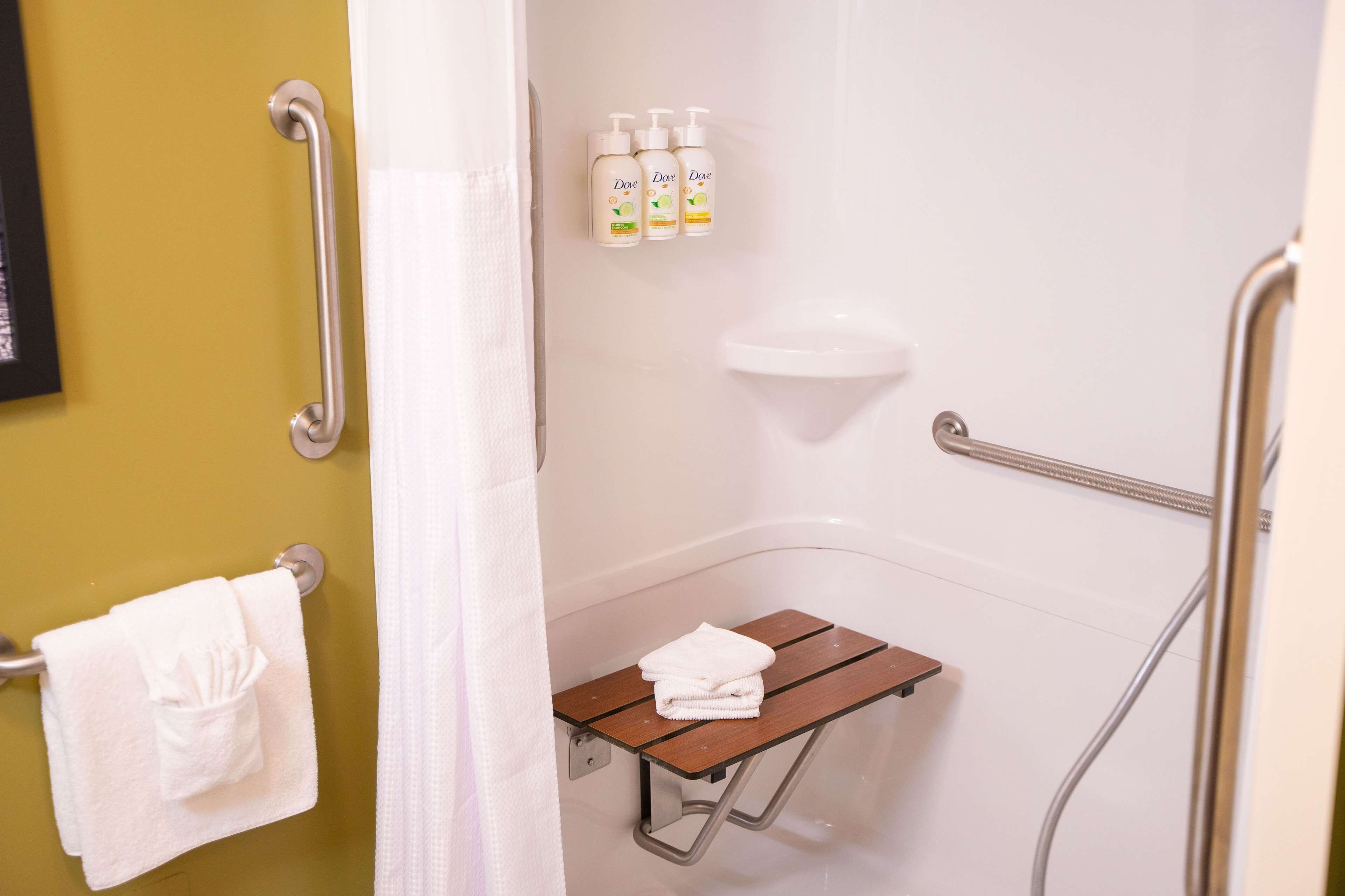 A bathroom with a shower, a grab bar, a small wooden shelf, and a towel rack.