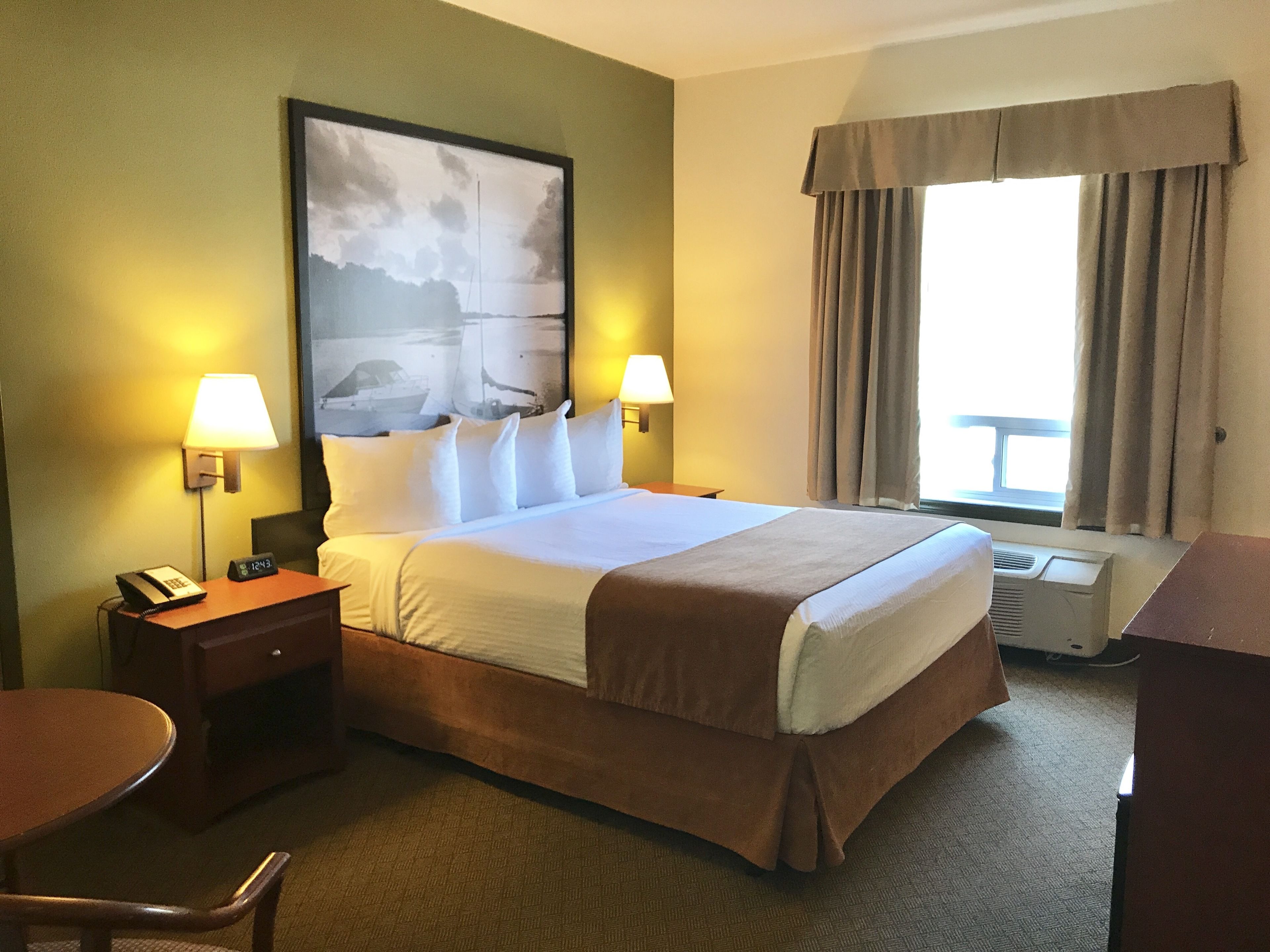 Habitación de hotel con una cama grande, dos lámparas de noche, un escritorio con teléfono, una silla y una ventana con cortinas.