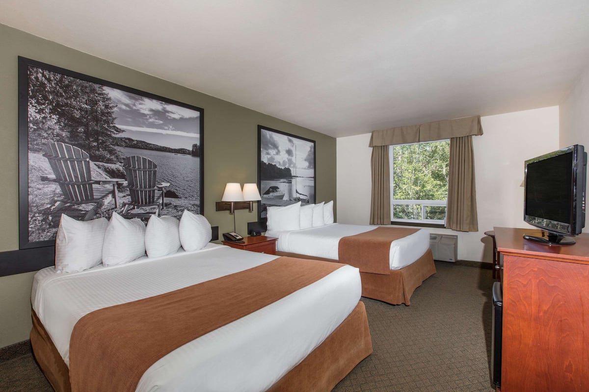 A hotel room with two beds, a television, a desk, and artwork on the walls.
