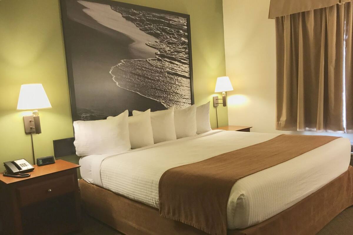A hotel room with a large bed, two bedside tables, a nightstand, a telephone, and a wall-mounted lamp.