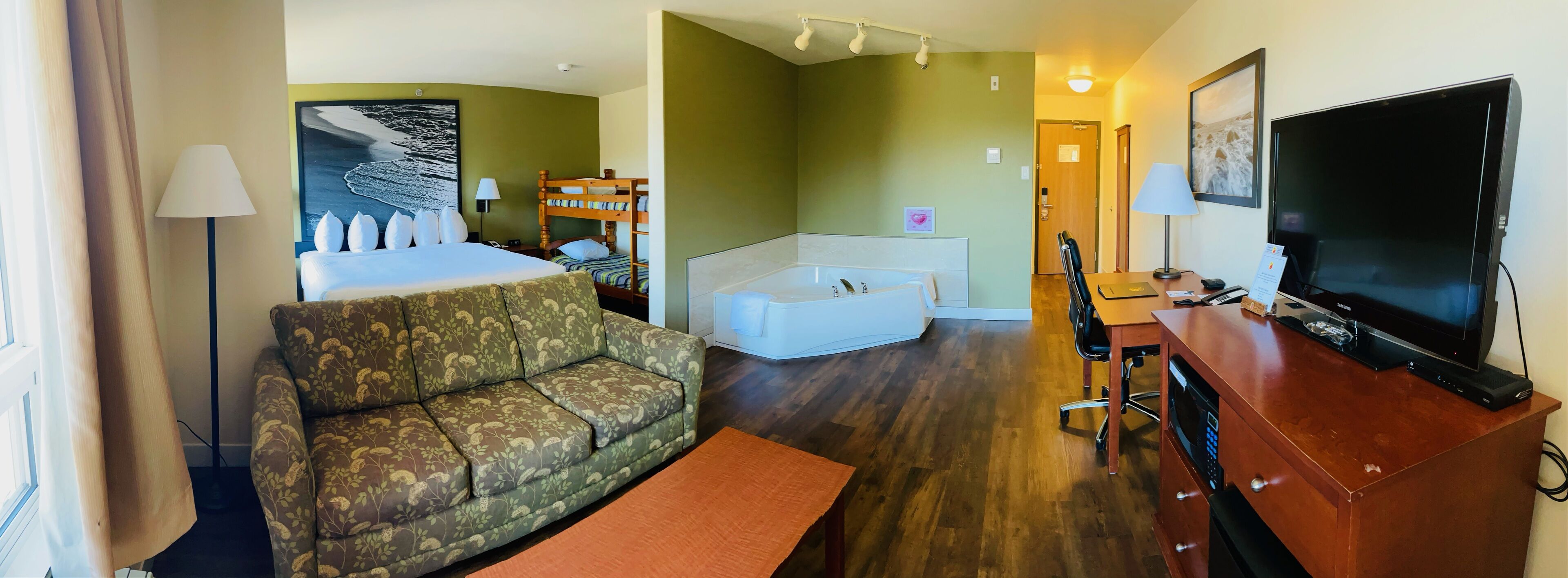 A hotel room with a sofa, a bed, a television, a desk, and a bathtub.