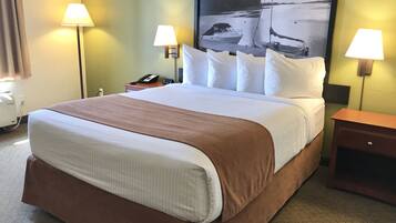 A hotel room with a large bed, two bedside lamps, a nightstand with a phone, and a painting of a boat on the wall.