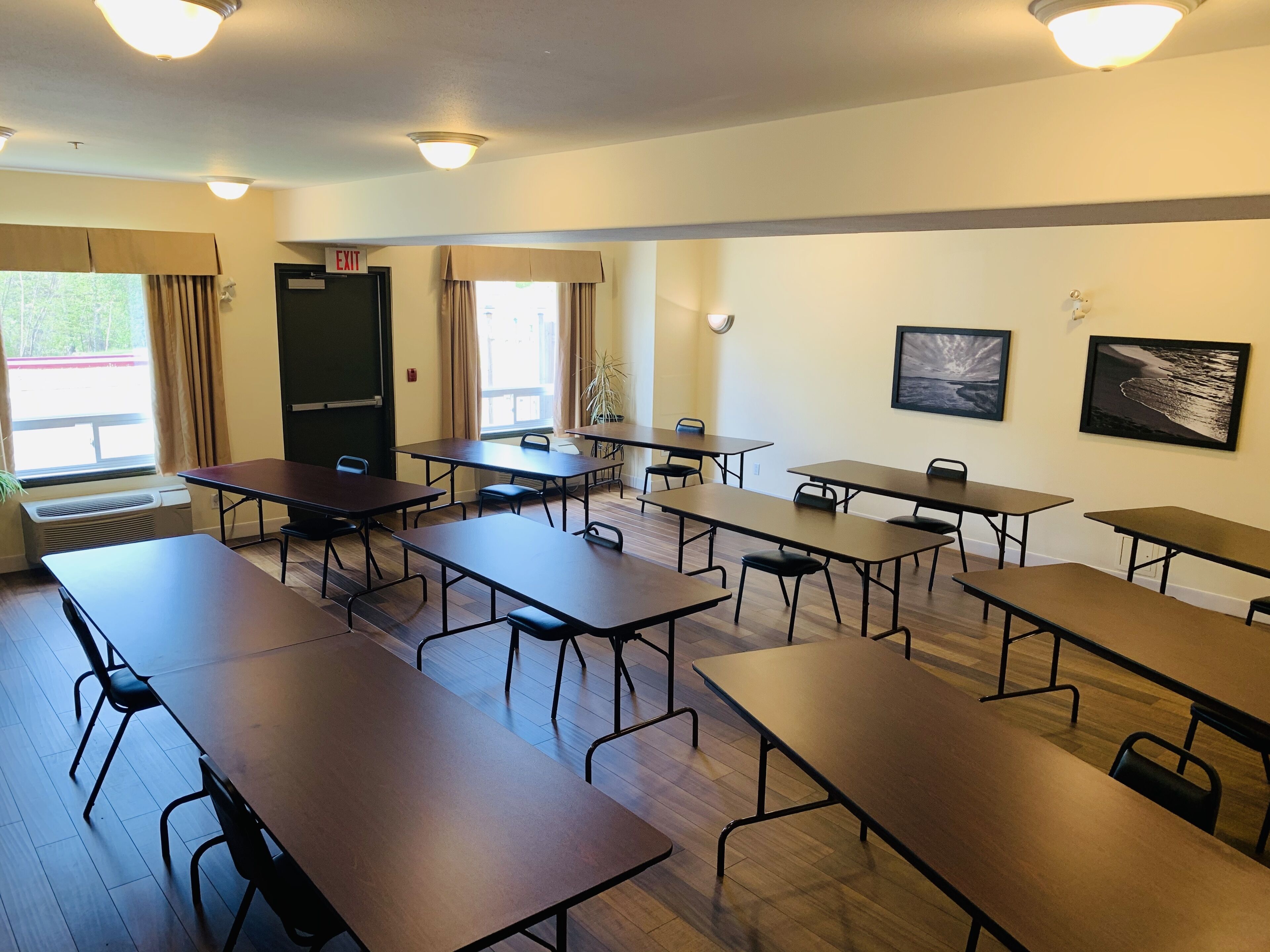 A conference room with multiple tables and chairs, a door marked "EXIT", and two windows with curtains.