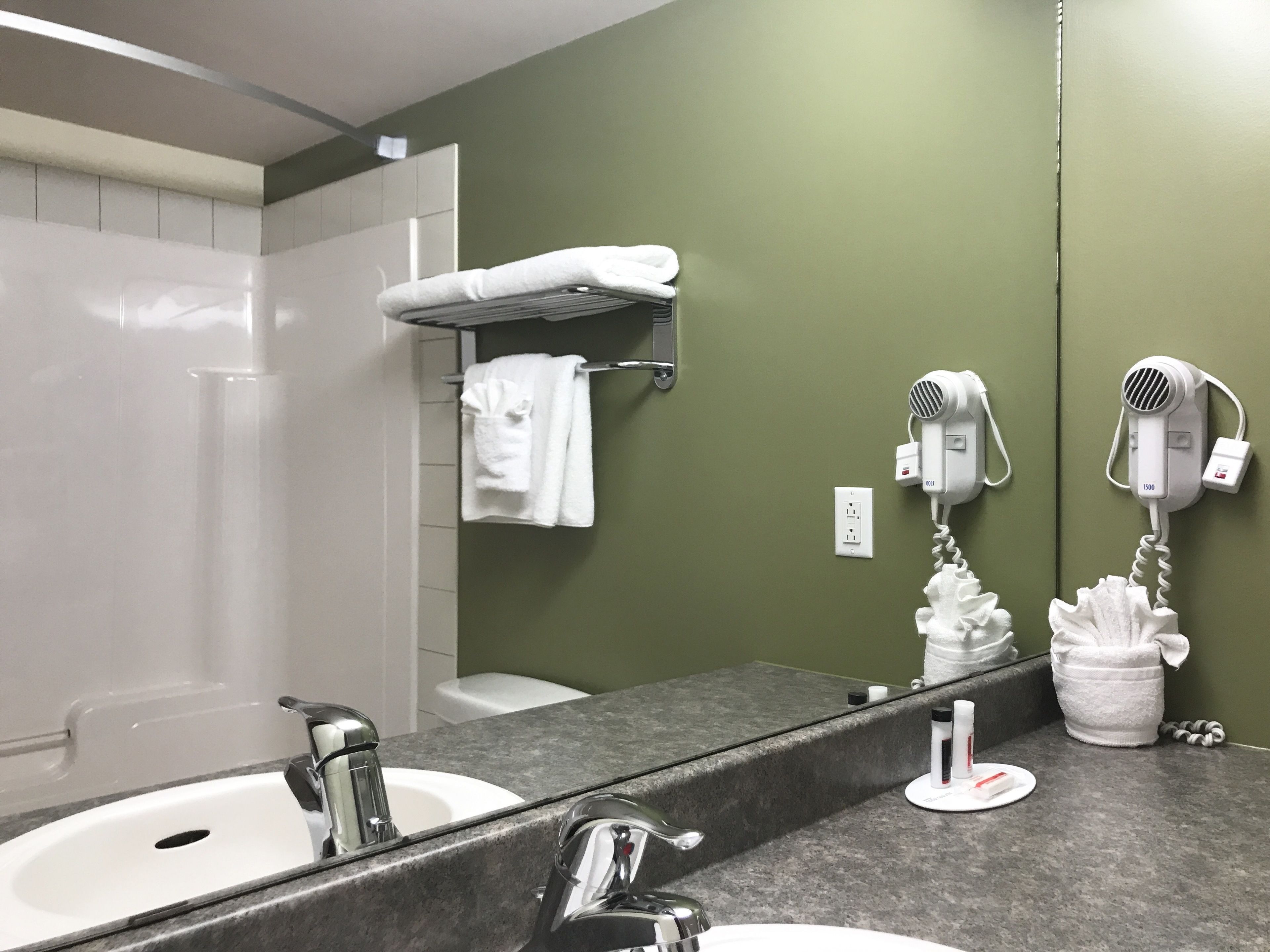 A bathroom with a large mirror, two sinks, a shower, and two hair dryers mounted on the wall.