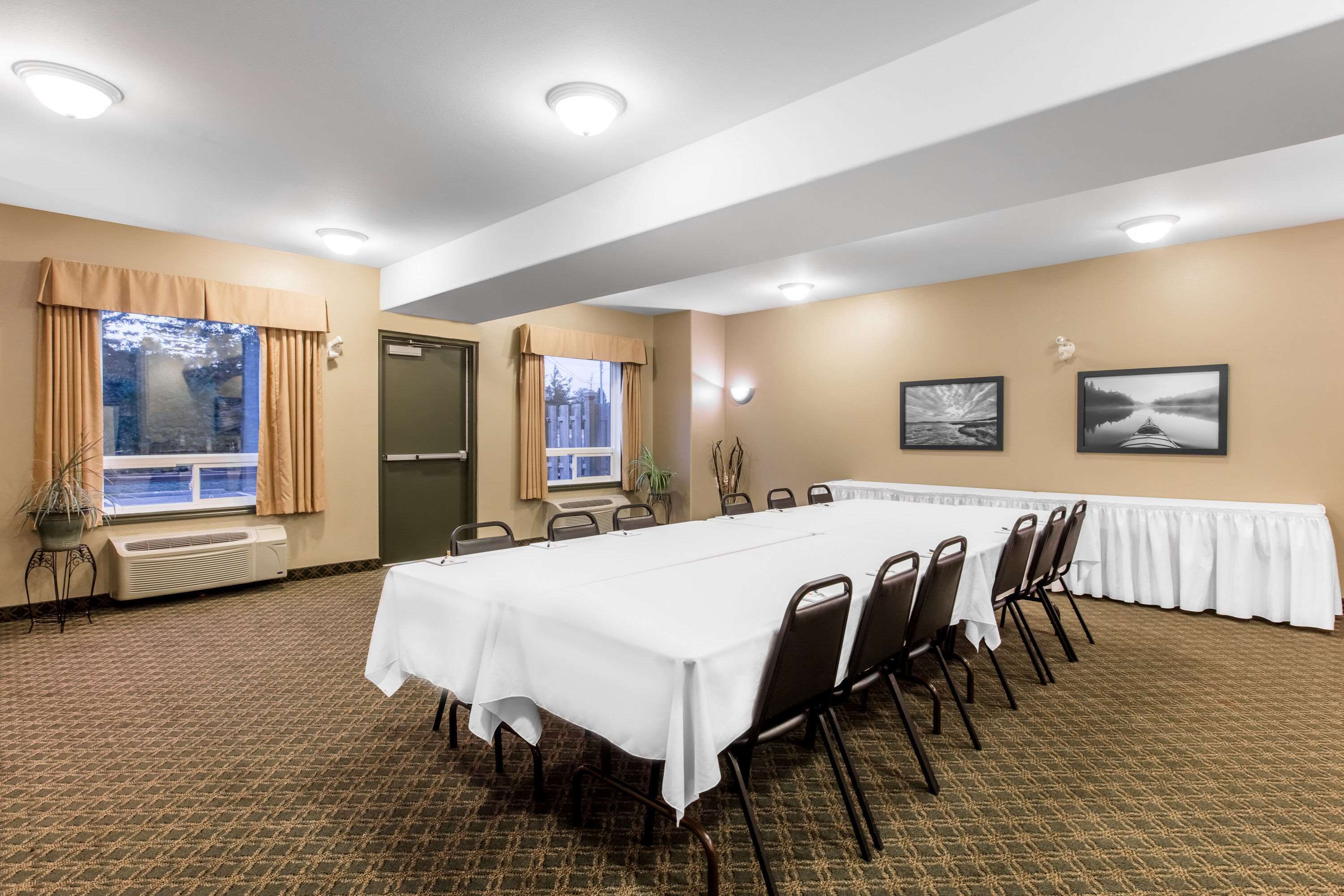 Un salón de conferencias con una larga mesa, sillas, una ventana con cortinas y dos cuadros en la pared.