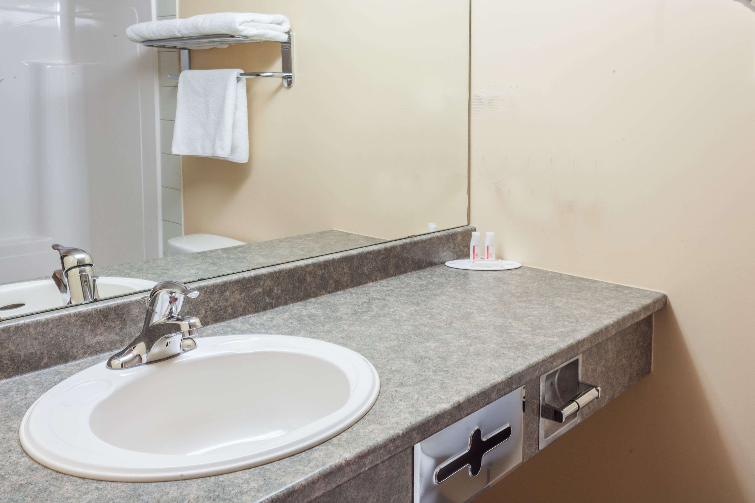 Un baño con lavamanos blanco, un espejo y un perchero para toallas.