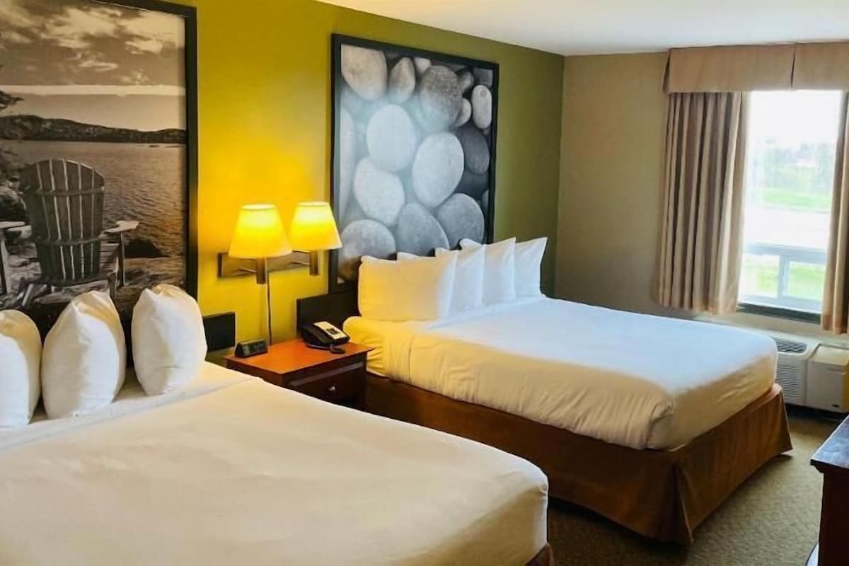 A hotel room with two beds, a painting, a lamp, and a window with curtains.