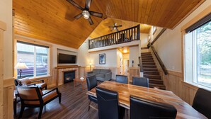 A spacious living area with a wooden ceiling, a dining table, and a staircase leading to an upper level. - Manning Park Resort (Manning Park)