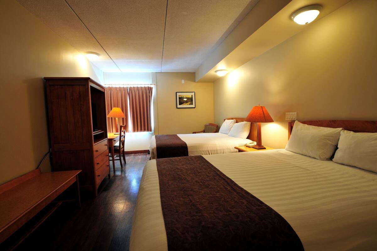 A hotel room with two beds, a wooden desk, a chair, a lamp, and a picture on the wall.