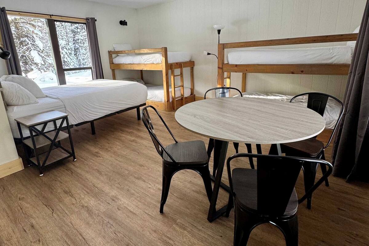 A room with bunk beds, a round table with chairs, and a window with curtains.