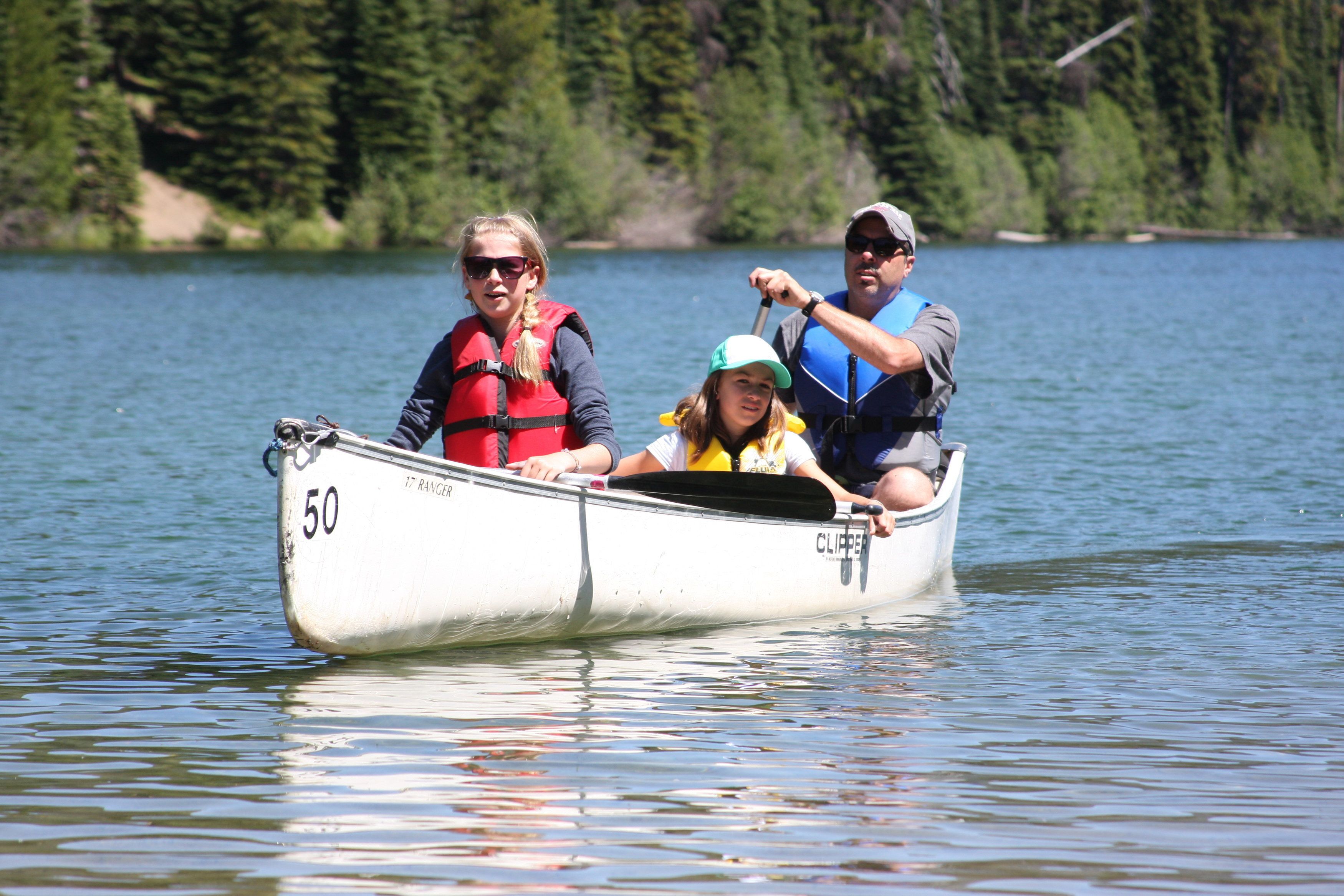 A canoe with three people on a calm lake surrounded by trees.