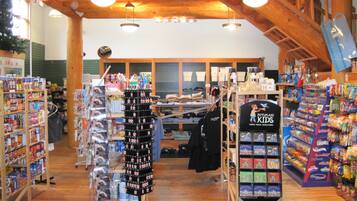 A store with wooden beams, shelves stocked with snacks, and a display of children's clothing.
