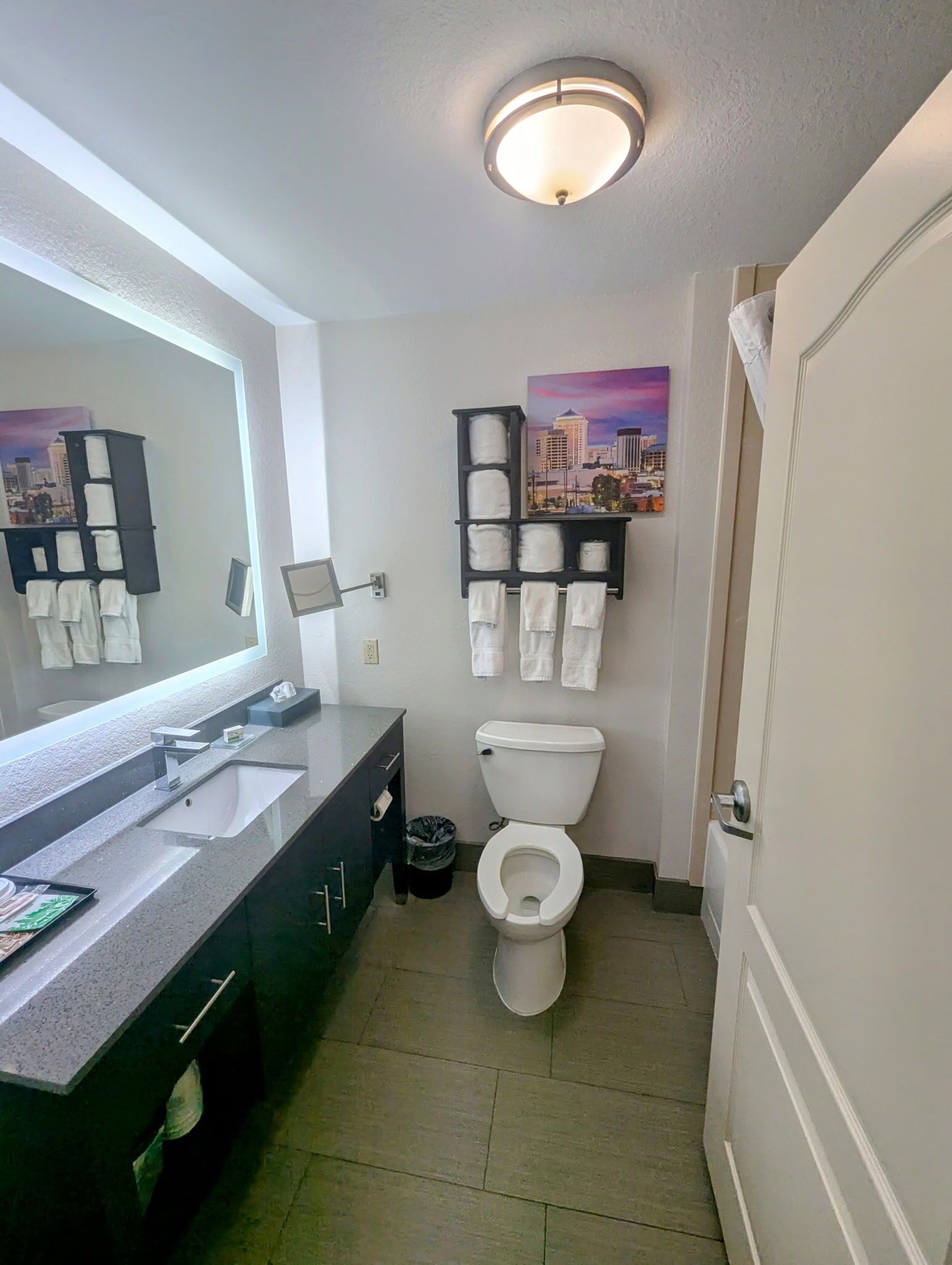 A modern bathroom with a large mirror, a sink, a toilet, and a towel rack.