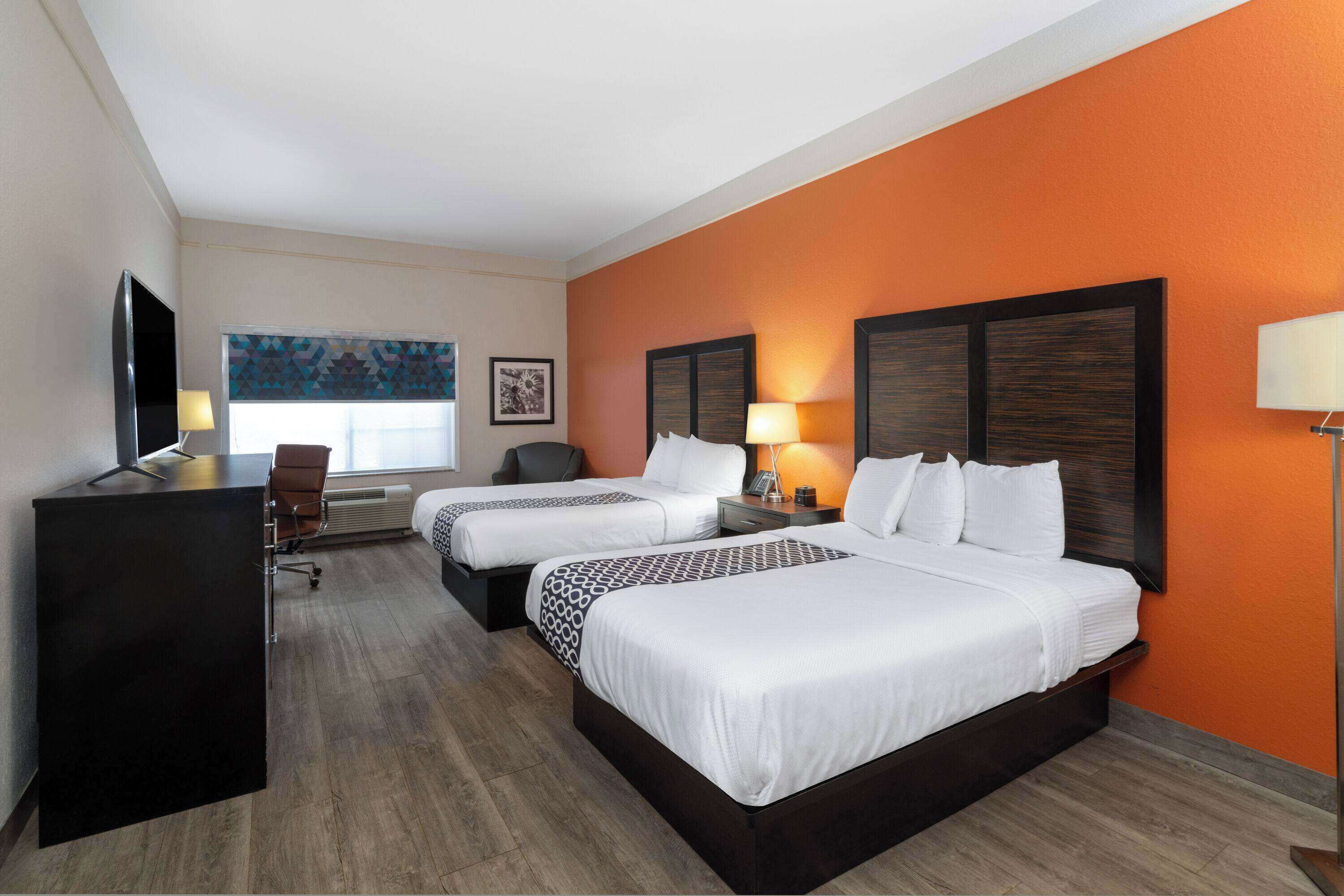 A hotel room with two beds, a desk, a chair, and a TV.