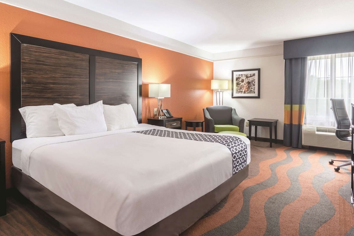 Une chambre d’hôtel avec un grand lit, un bureau, une chaise, une lampe et un tableau au mur.