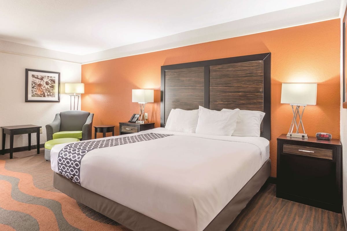 Une chambre d’hôtel avec un grand lit, deux tables de chevet, une chaise, un bureau et une lampe fixée au mur.