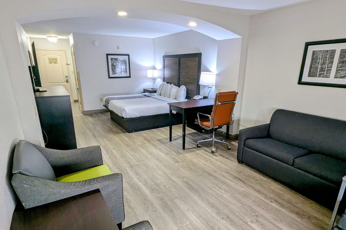 Une chambre d’hôtel moderne équipée d’un lit, d’un bureau, d’un fauteuil de bureau, d’un canapé et d’un petit fauteuil.