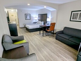 Quarto de hotel moderno com cama, escrivaninha, cadeira de escritório, sofá e uma poltrona.