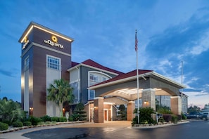 La Quinta's elegant entrance welcomes guests under a covered walkway, surrounded by lush landscaping and a majestic palm tree.