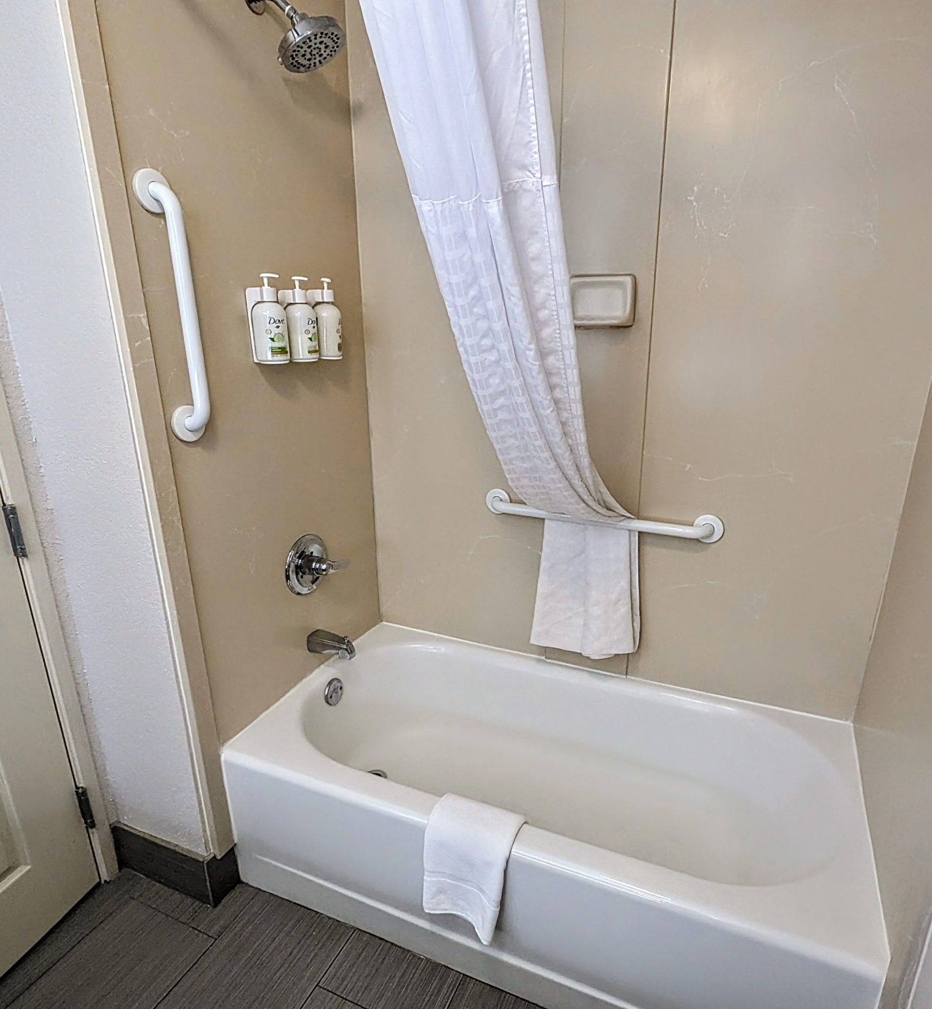 Un baño con bañera, cabezal de ducha, barras de apoyo y artículos de aseo.