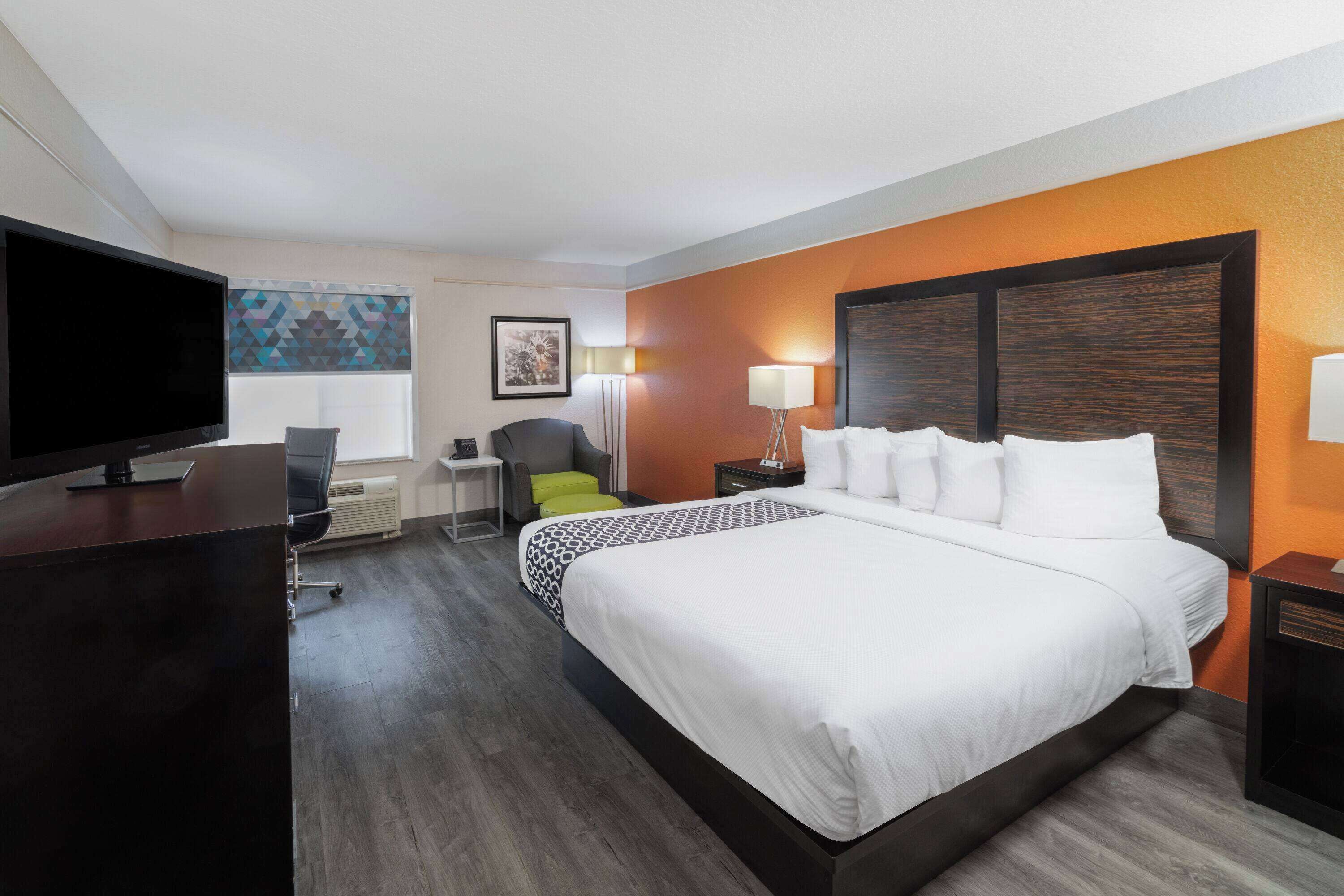 Habitación de hotel con una cama grande, un escritorio con televisor, una silla, una lámpara de escritorio y una ventana con cortinas estampadas.