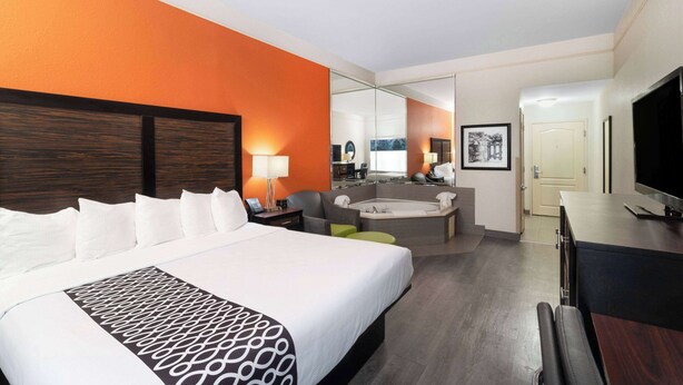 Een hotelkamer met een groot bed, een zithoek met een bank en fauteuil, een tafeltje, een televisie en een spiegel.