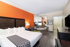 A hotel room with a large bed, a sitting area with a sofa and armchair, a small table, a TV, and a mirror. - La Quinta Inn & Suites by Wyndham Prattville (Prattville)