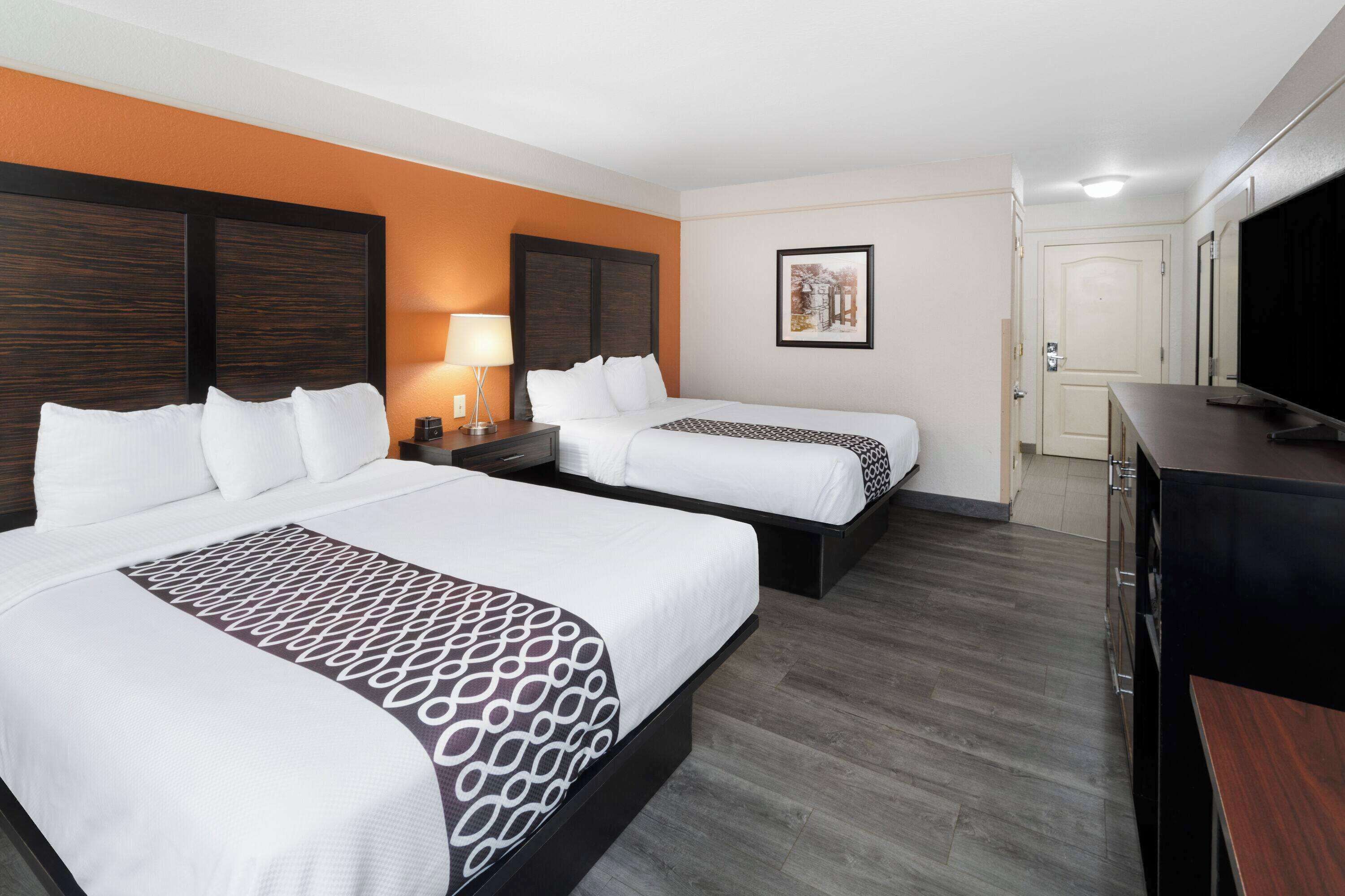 A hotel room with two beds, a TV, a desk, and a framed picture on the wall.