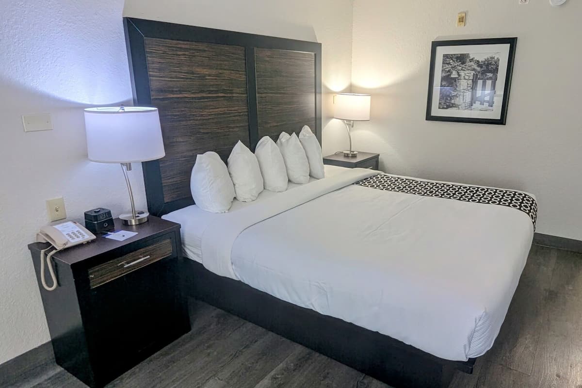 Une chambre d’hôtel avec un grand lit, une table de chevet avec une lampe, un téléphone et un tableau encadré au mur.