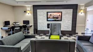 Een hotel lobby met een zithoek, een receptiebalie met computers en een grote televisie aan de muur.