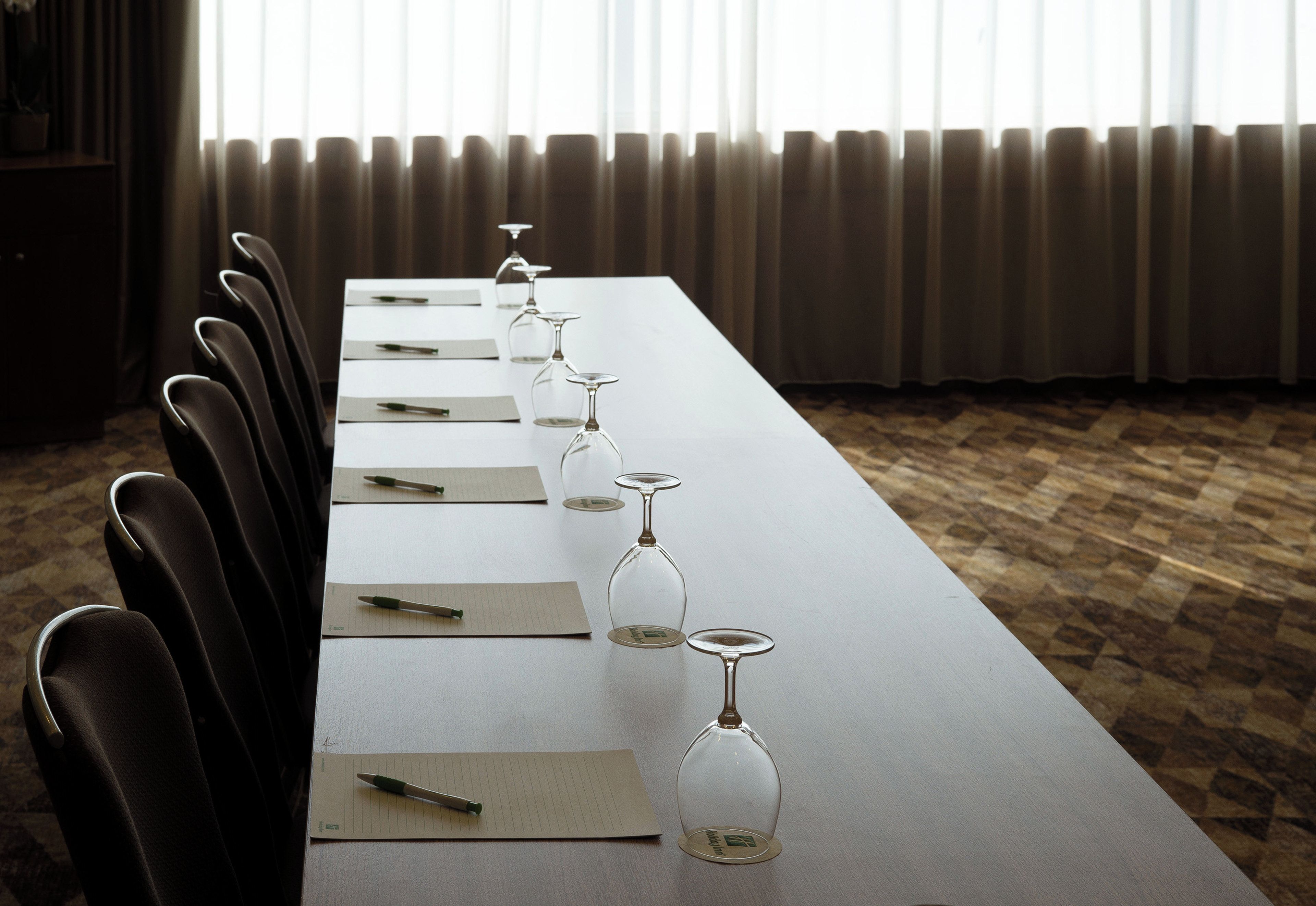 A conference room with a long table, chairs, and wine glasses set up for a meeting.