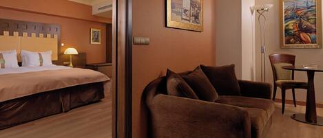 A hotel room with a bed, a sofa, a dining table, and two paintings on the walls.