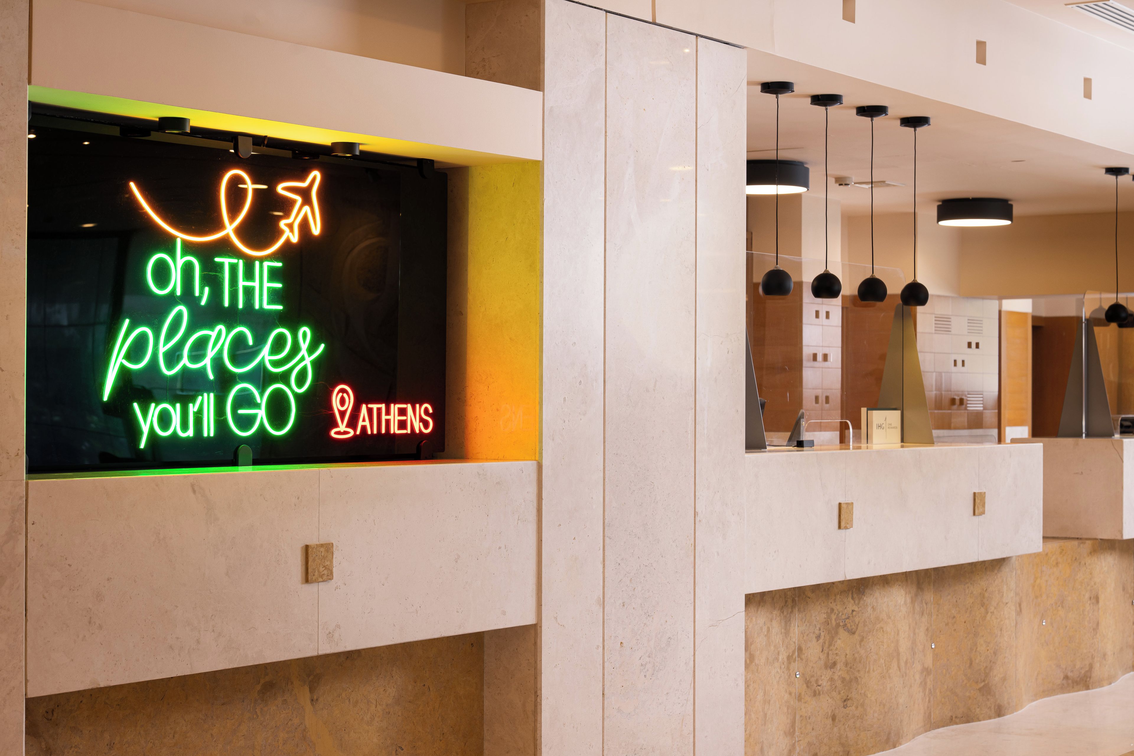 A modern hotel reception area with a neon sign, marble walls, and pendant lighting.