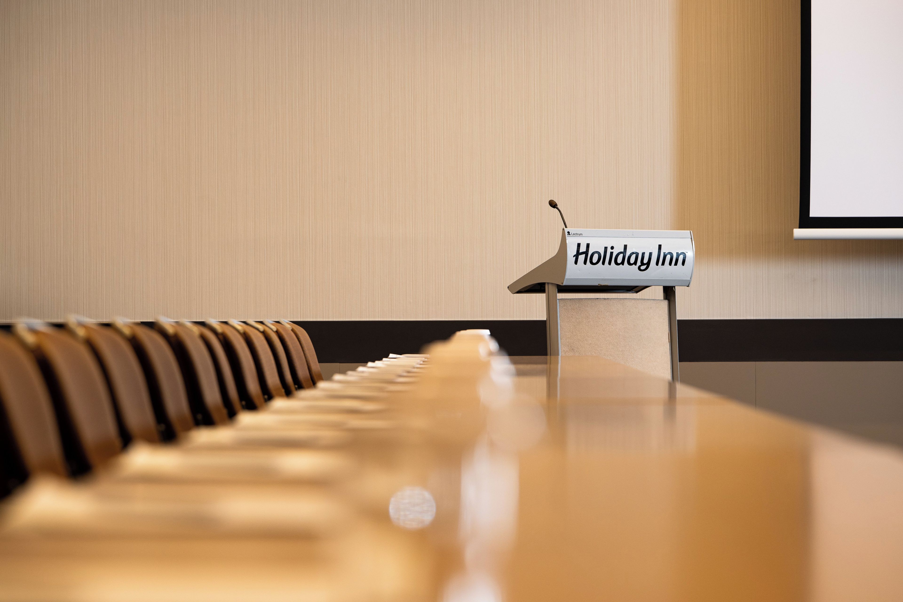 A piano with a sign reading 'Holiday Inn' in front of a wall with a projection screen.