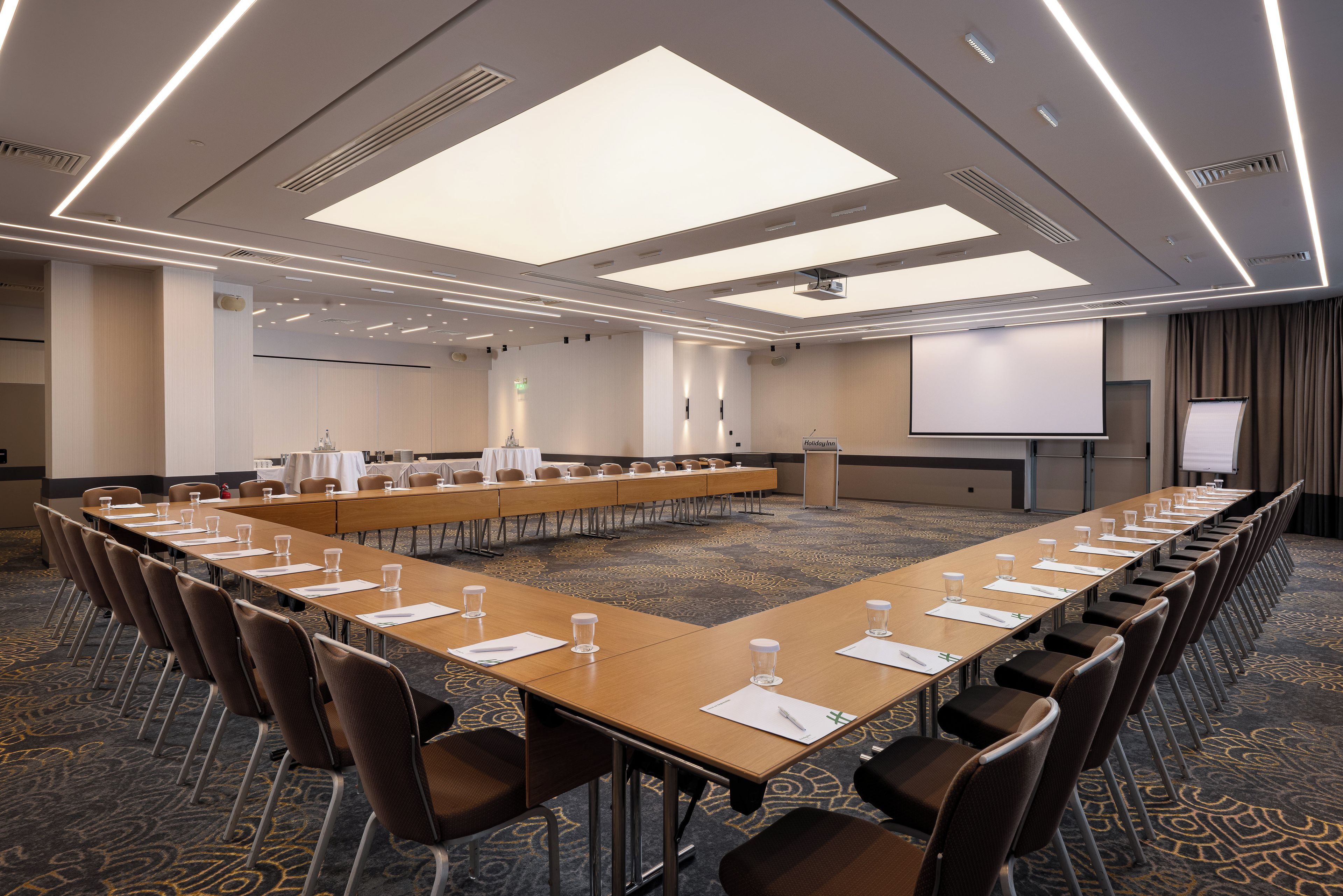 Un salón de conferencias con una larga mesa, sillas, una pantalla de proyector y una pizarra.