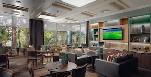 Un moderno salón de hotel con un televisor grande, asientos cómodos y vistas al exterior.