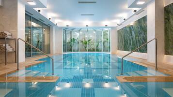An indoor swimming pool with glass walls, metal railings, and a tiled floor.