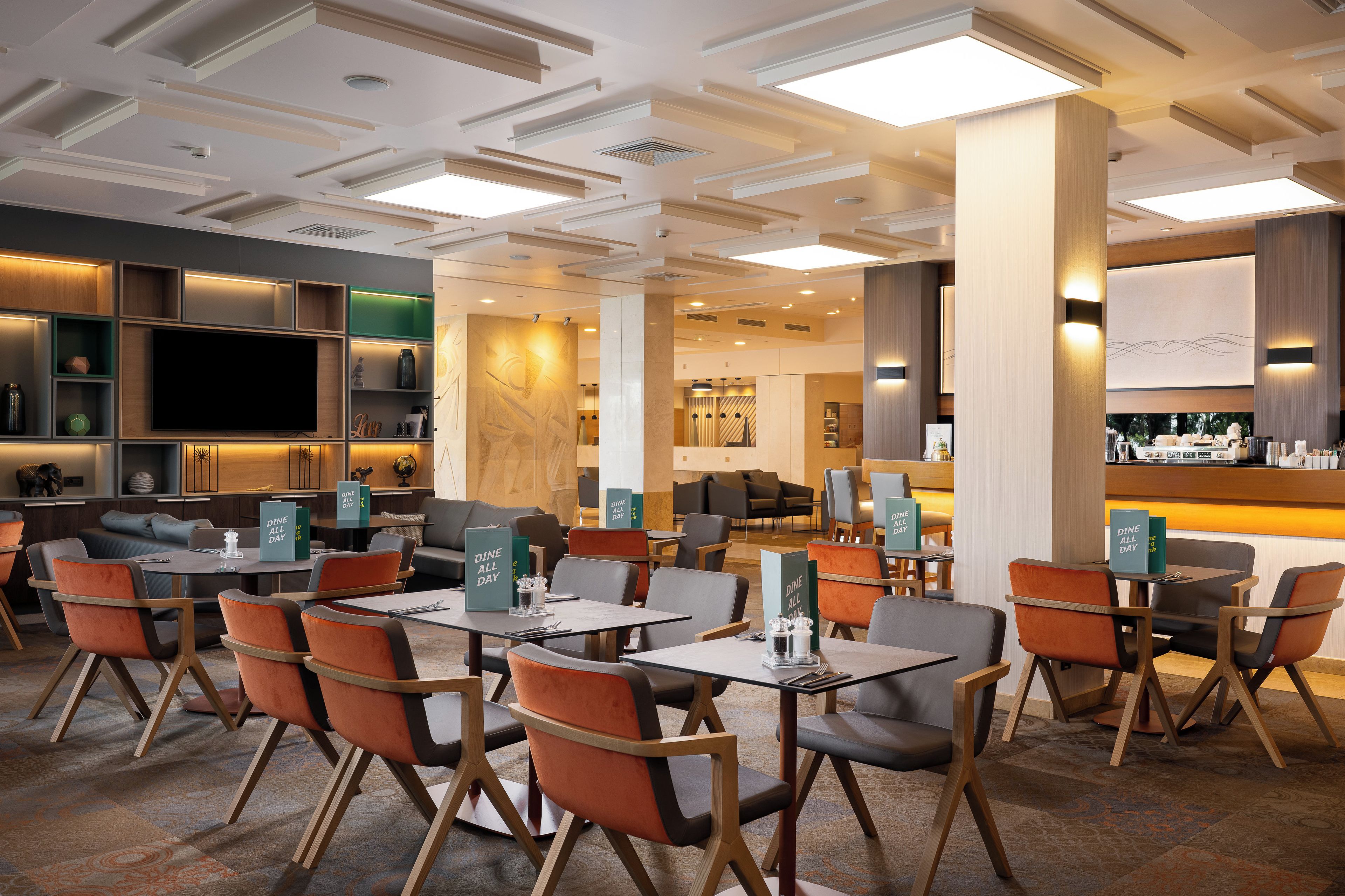 A modern hotel lobby with a dining area, seating arrangements, and a bar.