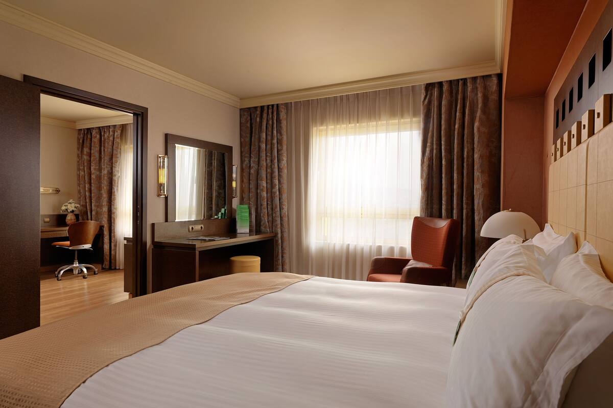 Een hotelkamer met een groot bed, een bureau, een stoel, een spiegel en een raam met gordijnen.