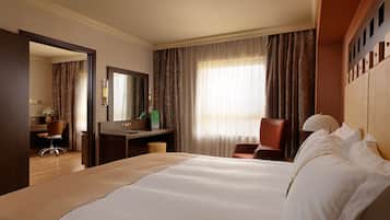 Habitación de hotel con una cama grande, un escritorio, una silla, un espejo y una ventana con cortinas.