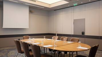A conference room with a long table, chairs, a projector screen, and a patterned carpet.